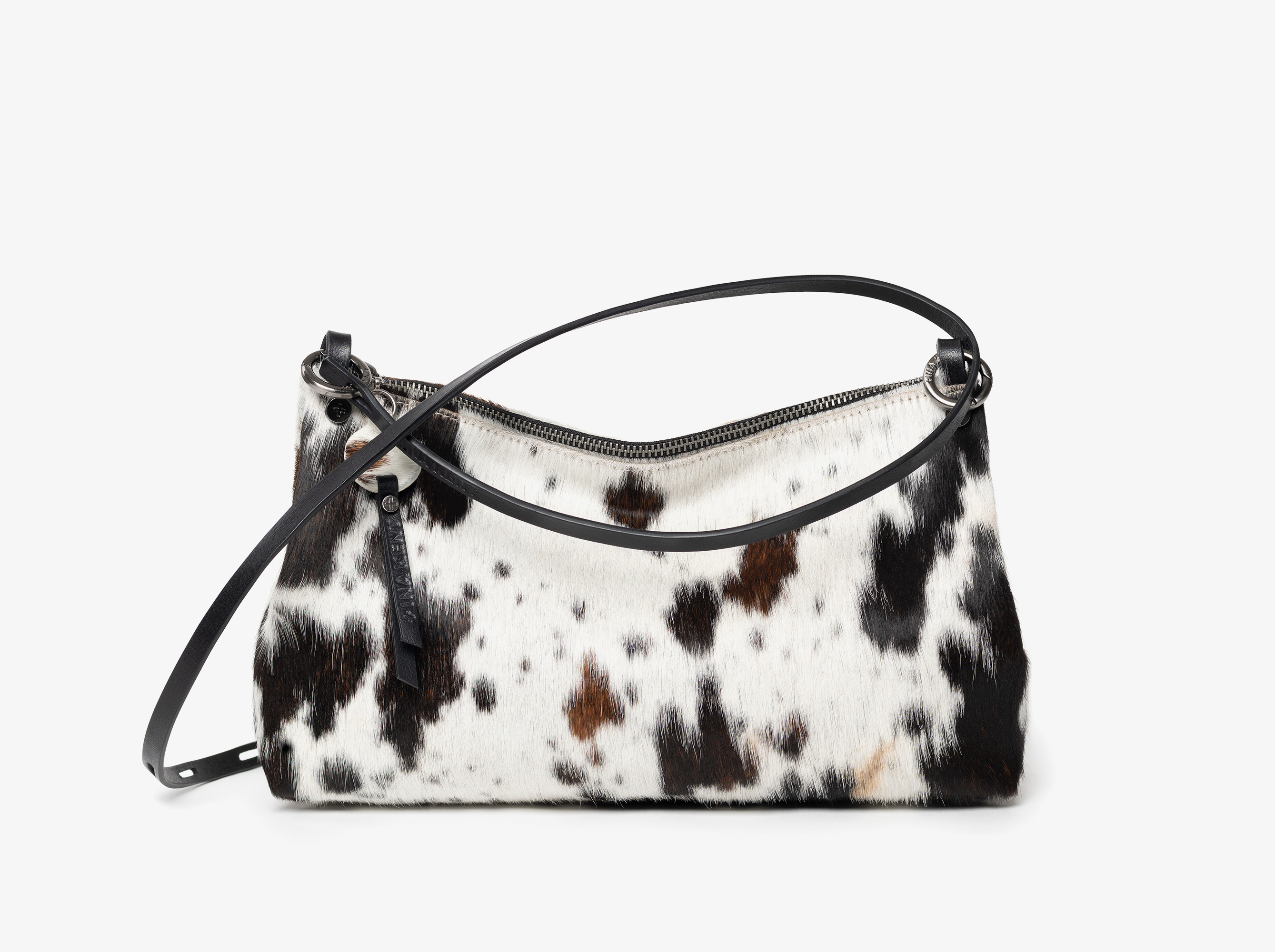 Rectangular handbag with black leather strap and zipper, featuring a black, brown, and white cowhide pattern on the exterior, set against a plain white background.