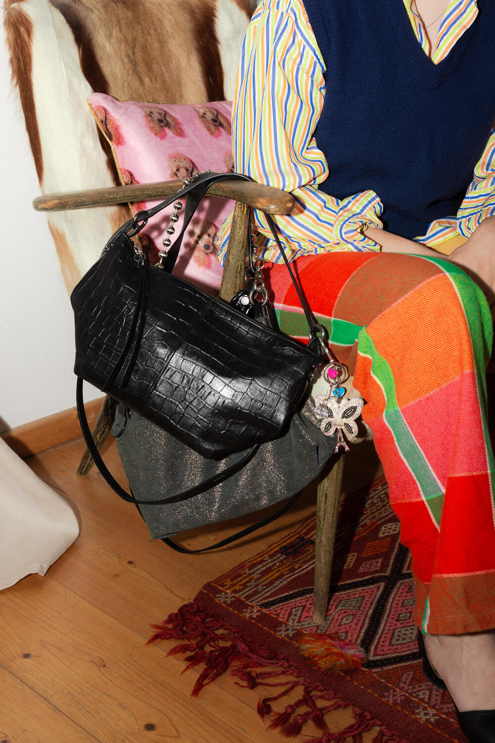 A person seated in a patterned chair with an INA KENT black handbag hanging on the armrest, surrounded by colorful textiles and pillows.