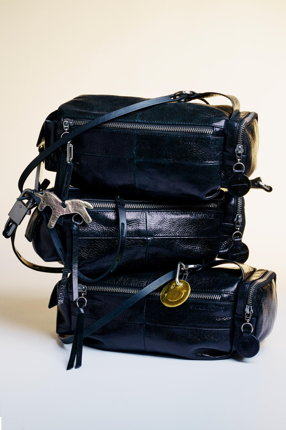 Drei schwarze Reisetaschen aus Leder von INA KENT sind übereinander gestapelt und jeweils mit metallischen Schlüsselanhängern und Anhängern verziert.