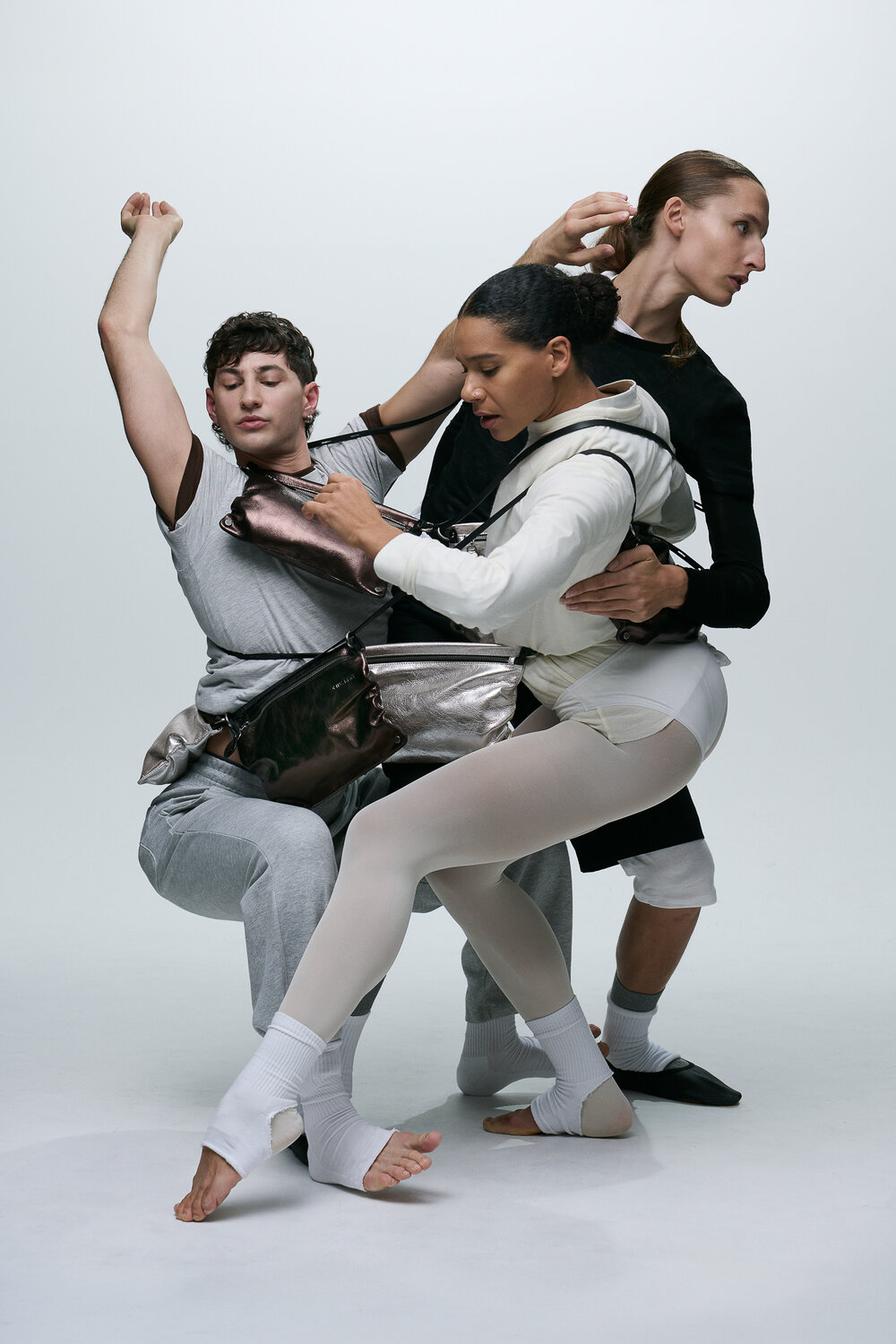 Three dancers in athletic and casual clothing, featuring stylish INA KENT accessories, perform a contemporary pose together against a plain white background, each striking expressive and intertwined positions.