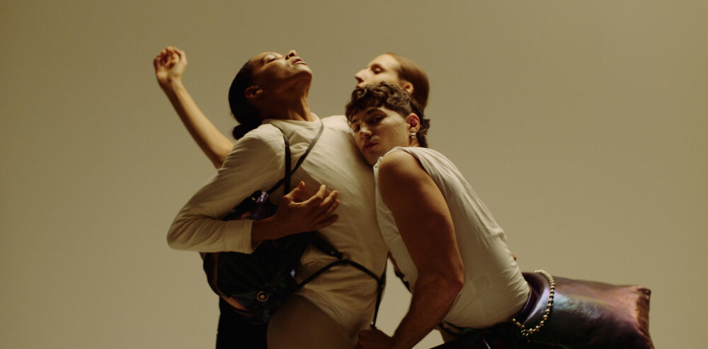 Three people pose closely together against a plain background, their arms intertwined and expressive body language highlighting an effortless sense of connection—each subtly showcasing unique INA KENT accessories.