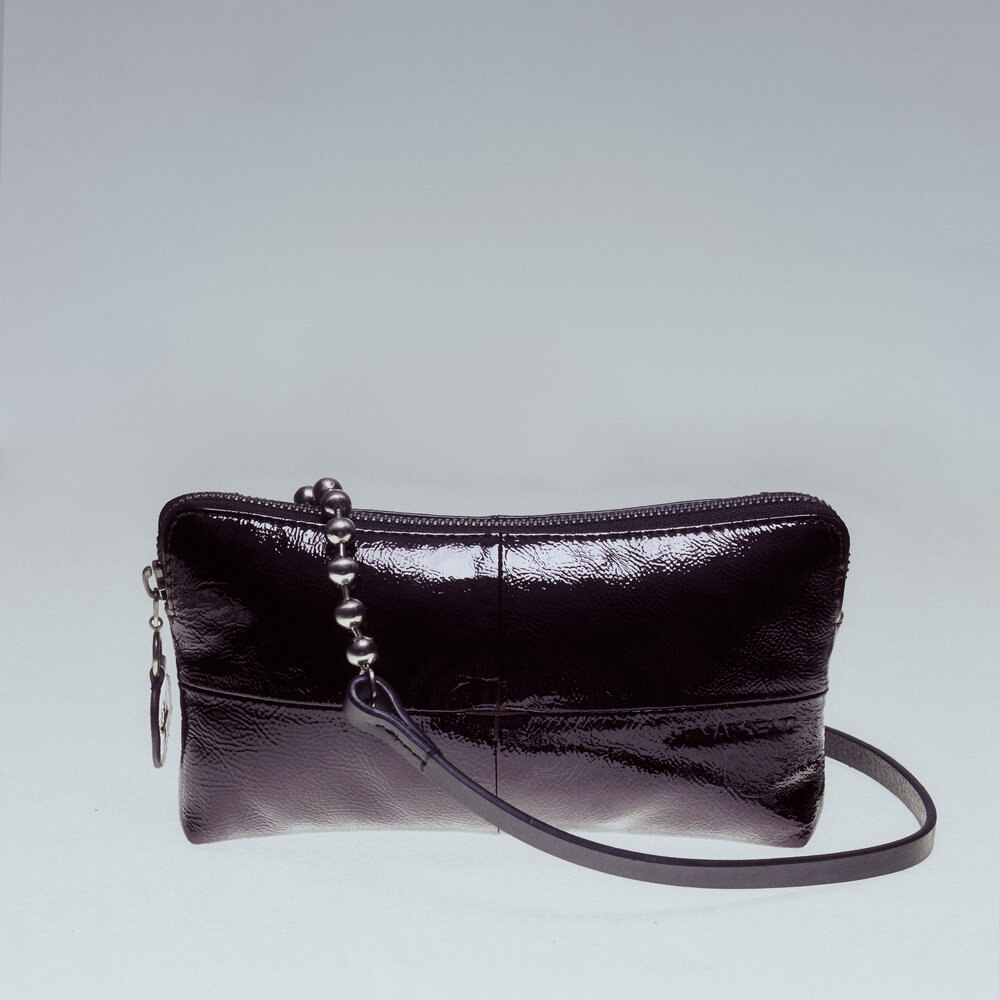 A small, glossy black leather INA KENT crossbody bag with a zipper closure and a thin shoulder strap is showcased against a plain background.