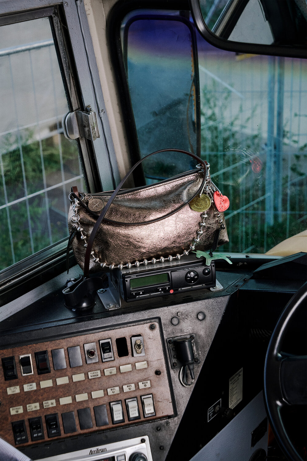 A metallic INA KENT purse with keychains and coins sits on the control panel inside a vehicle, next to various buttons, switches, and a radio.
