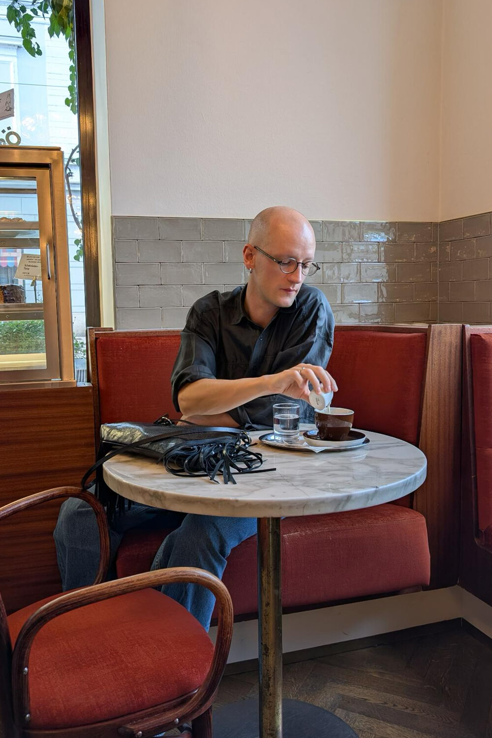 Eine Person, die an einem kleinen Cafétisch sitzt, gießt Milch in eine Tasse Kaffee.