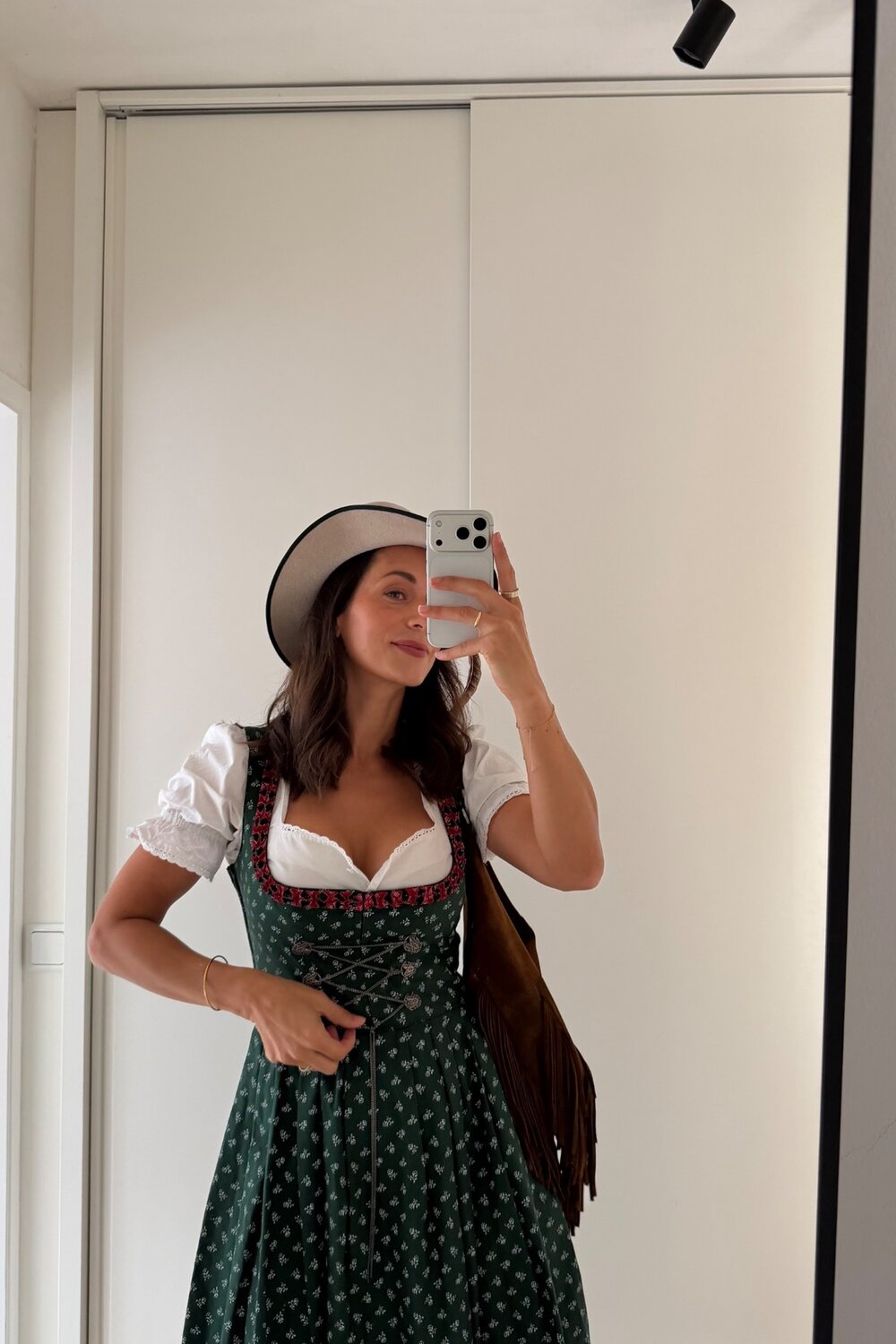 Eine Frau, die ein traditionelles grünes Dirndl und einen Hut von INA KENT trägt, macht ein Spiegel-Selfie.