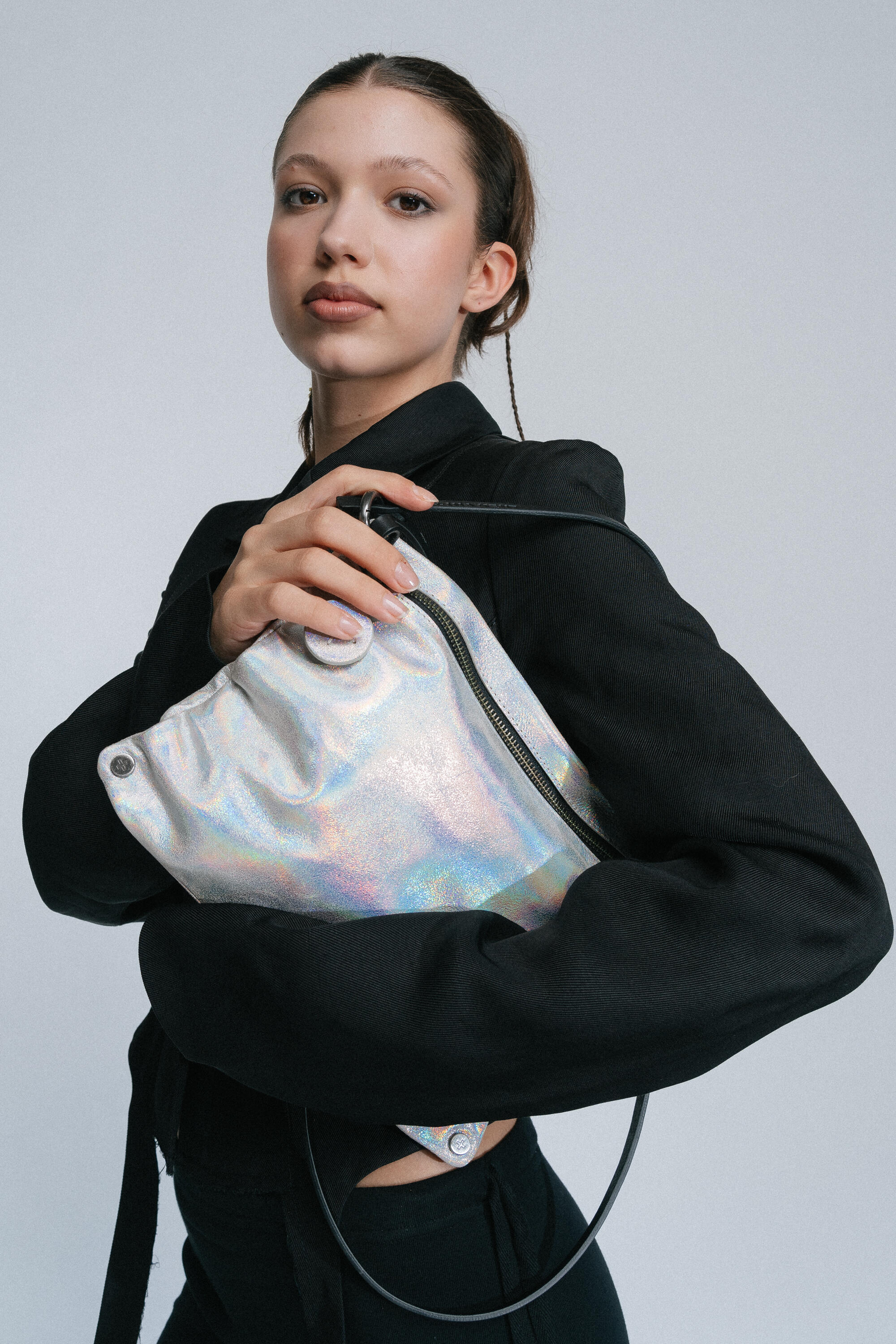 A person in a black outfit holds an INA KENT holographic bag close to their chest against a plain backdrop.