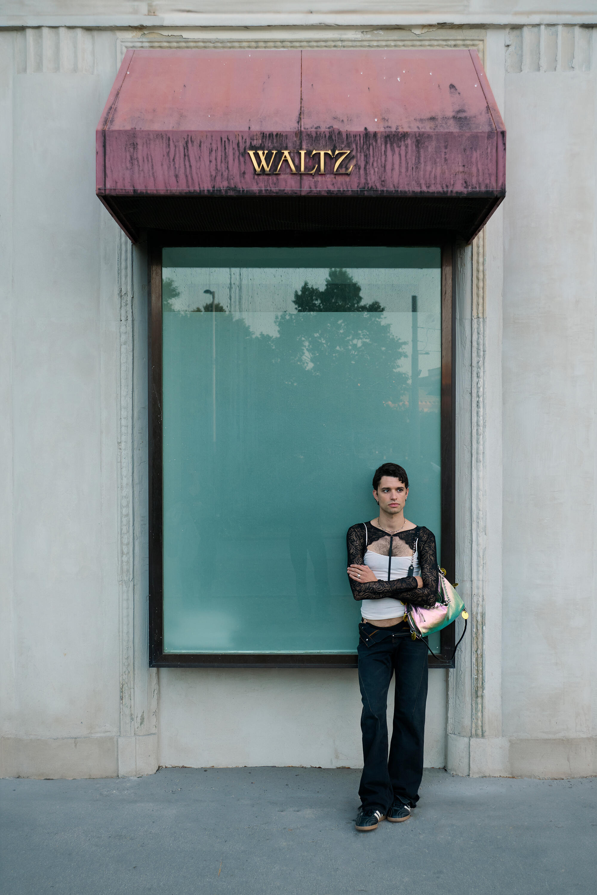 A person stands in front of a large window with a red awning labeled "WALTZ," holding INA KENT items and looking at the camera.