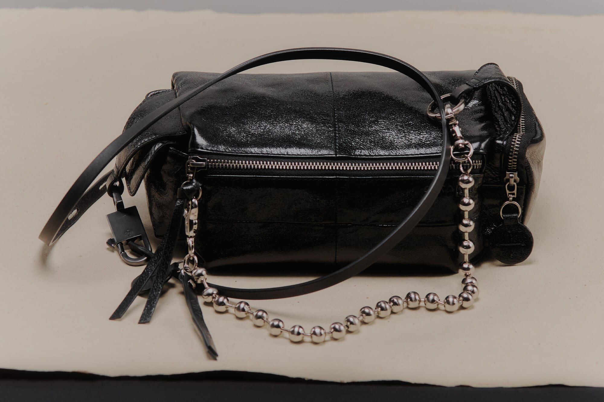 An INA KENT black leather handbag with a front zipper, decorative tassels, and a chain strap featuring round metallic beads, elegantly placed on a neutral background.