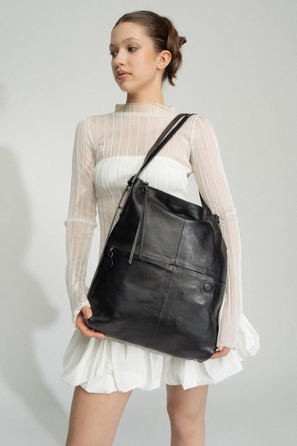 Frau in weißer Langarmbluse und Rock hält eine große schwarze Lederhandtasche mit Schulterriemen von INA KENT.