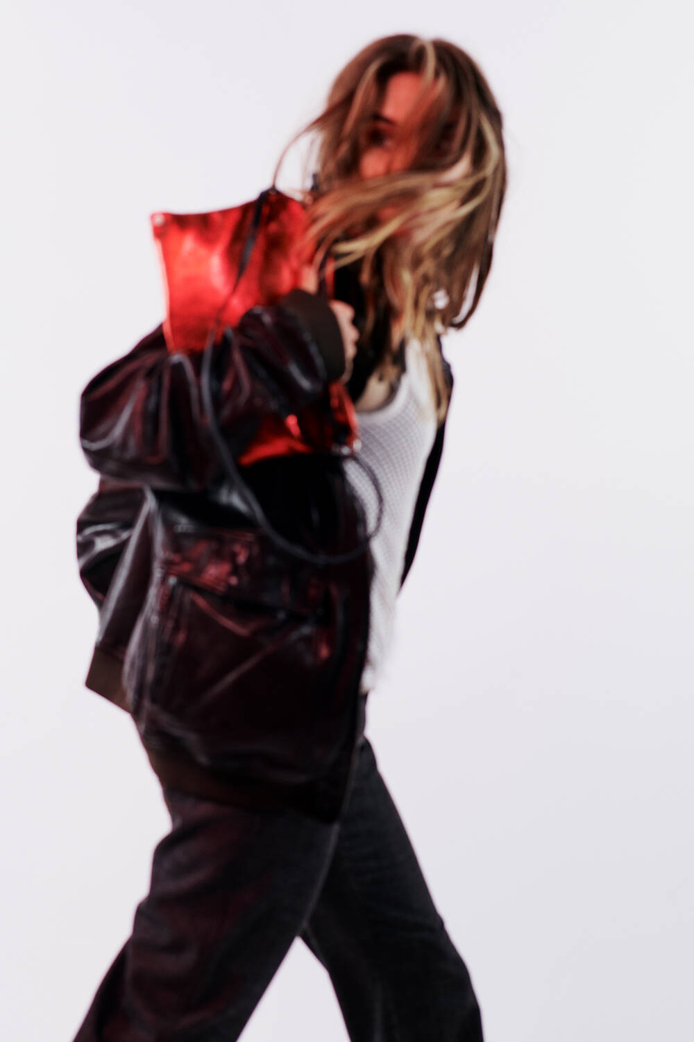 Person wearing a stylish black jacket and holding a chic INA KENT red bag, striding with dynamic motion against a plain white background.
