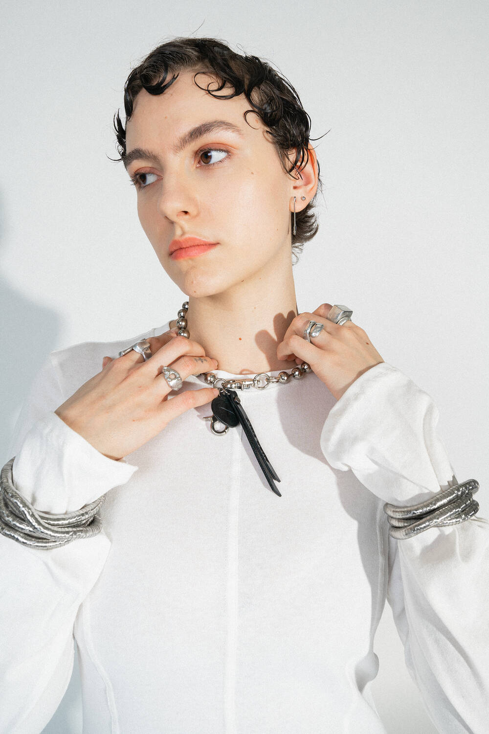 BALL'N'CHAIN metallic deep tar (worn as a necklace): A silver ball chain, creatively worn as a necklace, combined with a white top. The chain is decorated with a small black leather tag.