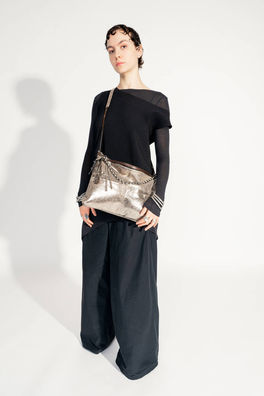 Model mit INA KENT ROVE ed.3 metallic bright anthra (schräg, von der Seite getragen): Die Tasche wird über die Schulter getragen und zeigt ihre klare Form sowie die schimmernde Oberfläche. Das Model trägt ein elegantes schwarzes Outfit.