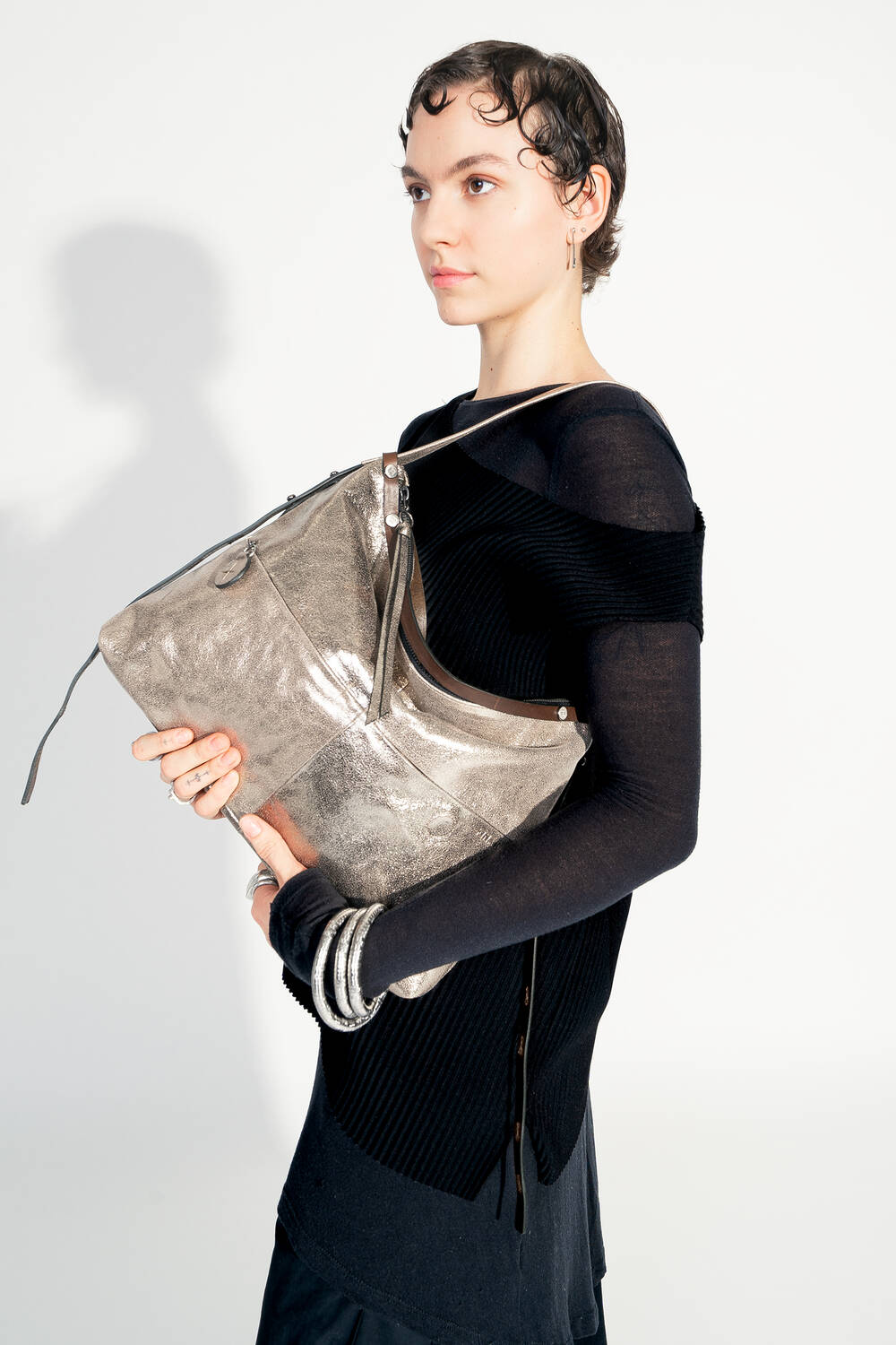 Model mit INA KENT ROVE ed.3 metallic bright anthra (in der Hand, Frontalansicht): Das Model hält die Tasche mit beiden Händen vor sich, wodurch die glänzende metallic-anthrazitfarbene Oberfläche und die praktische Größe betont werden. Die Tasche wirkt modern und vielseitig.