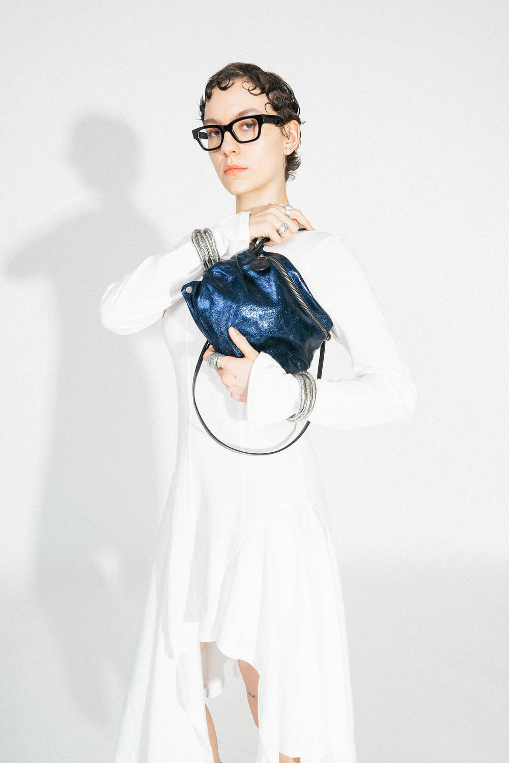 Close-up of the MOONLIT ed.1 in Crackled Deep Navy, held in the wearer's hand. The texture of the bag becomes more visible and emphasizes the metallic surface. It is carried by a black, narrow strap.