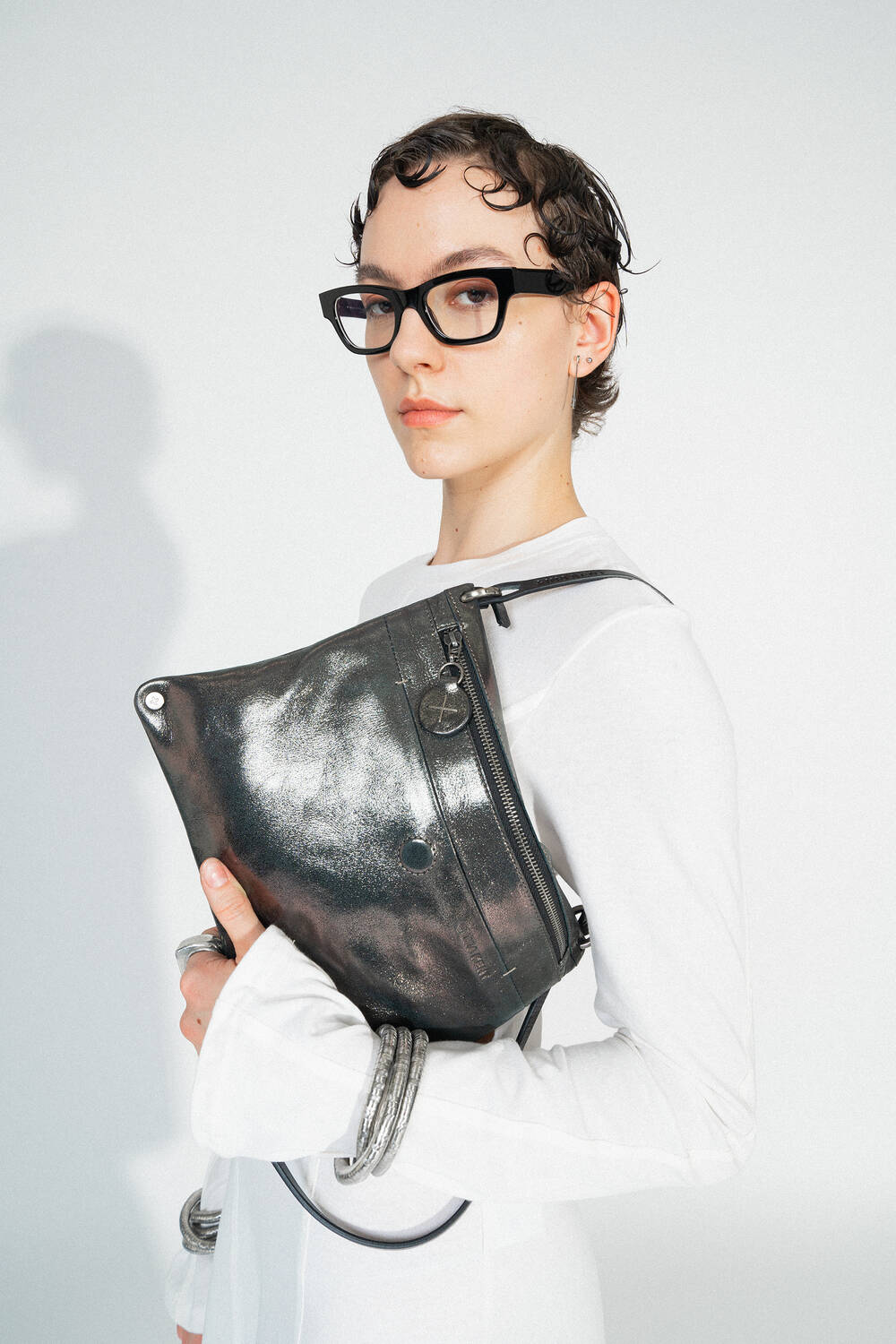 INA KENT MOONSTRUCK ed.1 crackled graphite (Detailaufnahme): Nahaufnahme der Tasche, die von einer Hand gehalten wird. Der Fokus liegt auf der strukturierten Lederoberfläche, dem dezenten Reißverschluss und dem schwarzen Riemen.