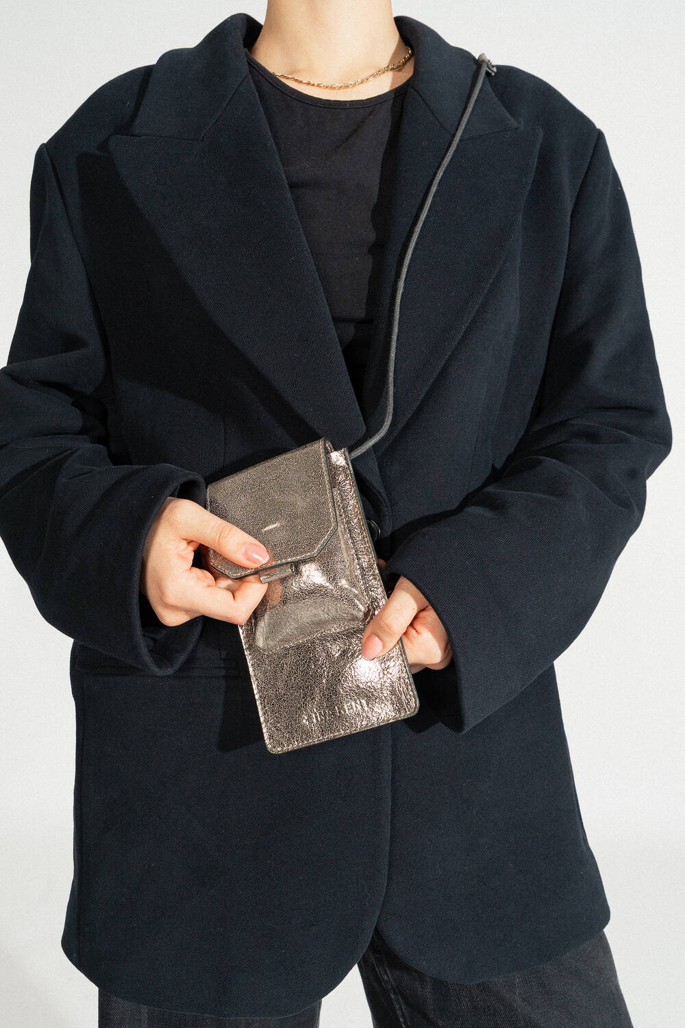 A person in a dark coat holds an INA KENT metallic silver handbag set against a neutral background.