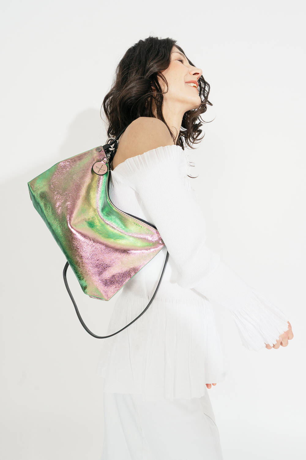 Person in a white off-shoulder outfit carrying an INA KENT iridescent bag over their shoulder against a plain background.