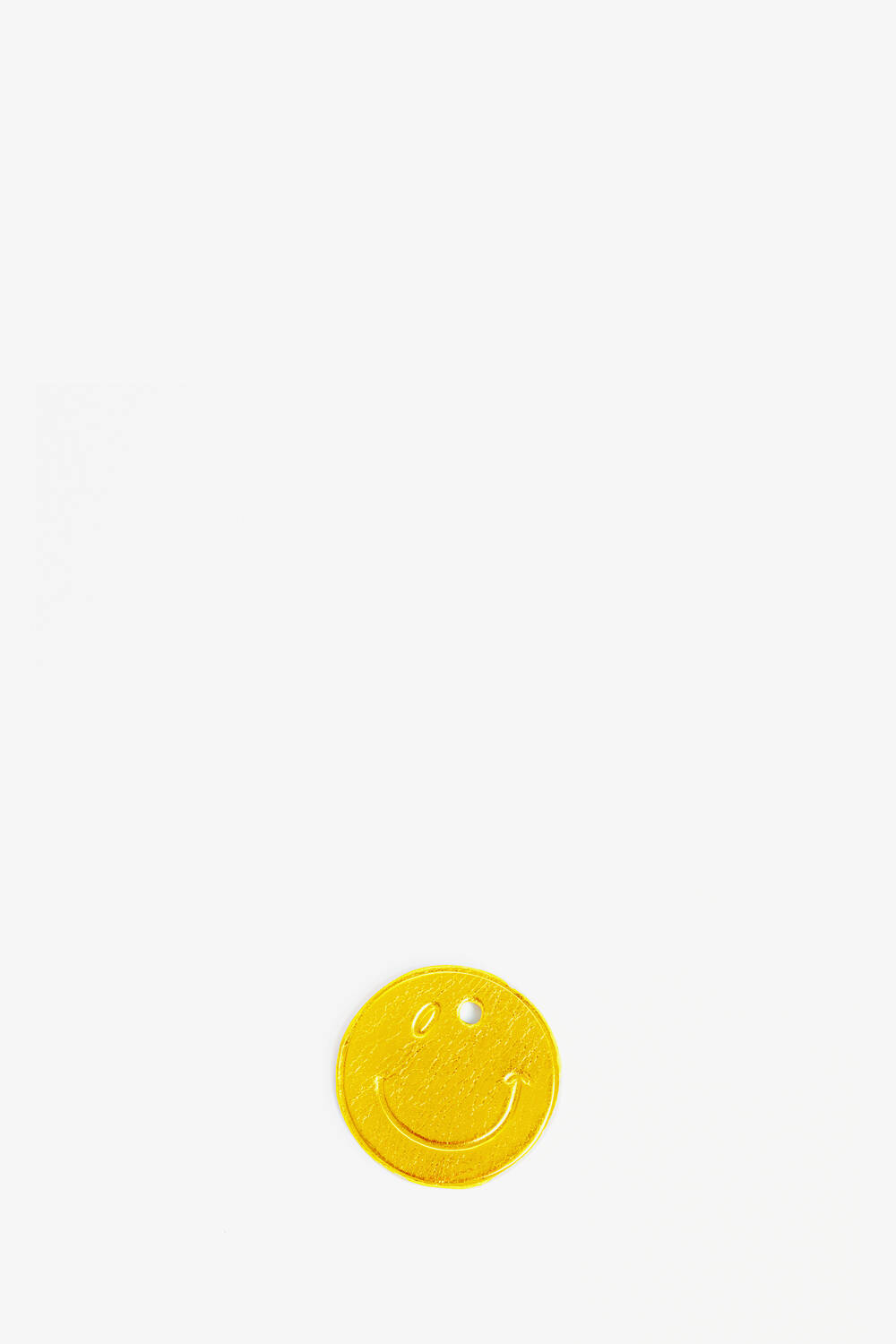 Auf einem schlichten weißen Hintergrund liegt ein gelbes rundes Etikett von INA KENT mit einem geprägten Smiley und einem kleinen Loch oben.