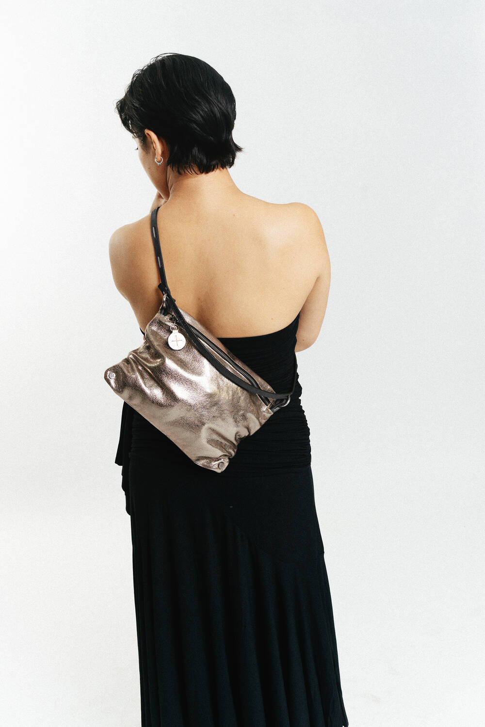 Eine Frau mit kurzen dunklen Haaren, die ein schwarzes, schulterfreies Kleid trägt, steht mit dem Gesicht nach hinten und trägt eine metallene INA KENT-Umhängetasche.