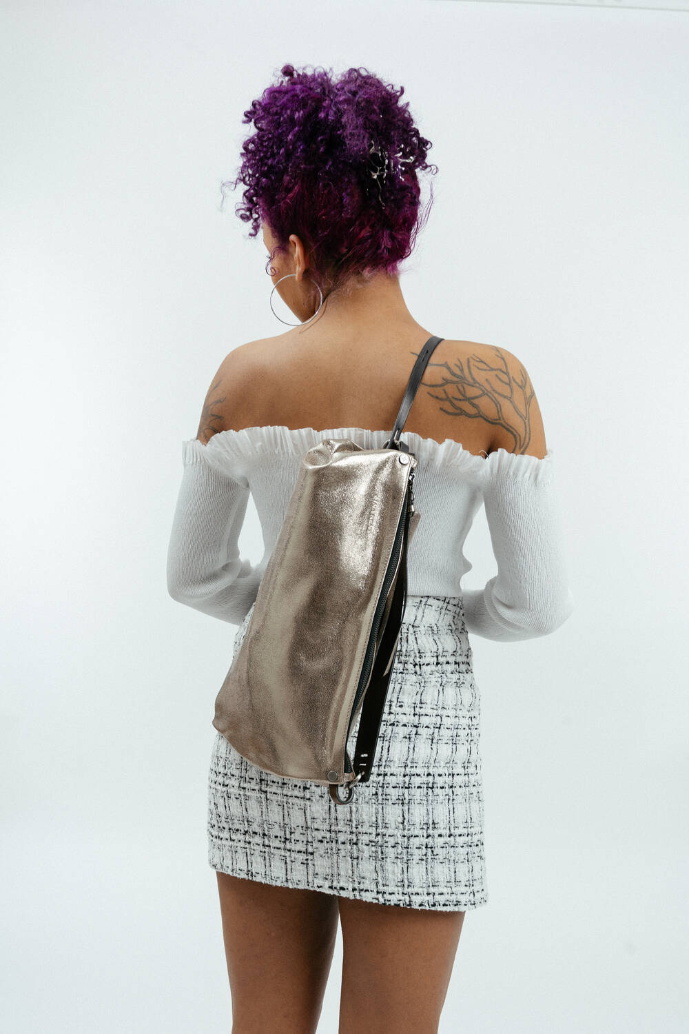 Weiblich gelesene Person mit goldenem Seesack mit schwarzem Riemen am Rücken