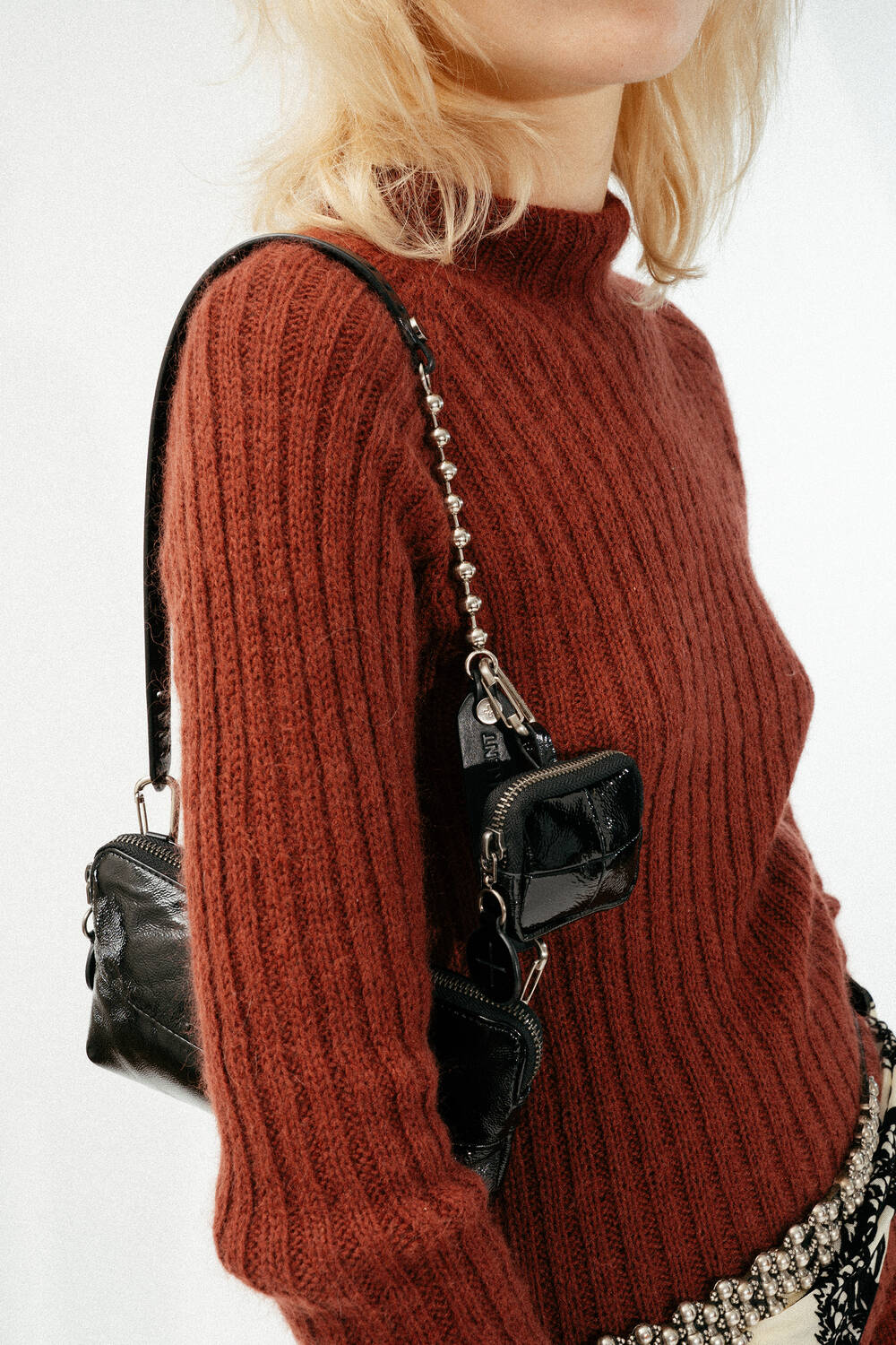 Eine Person, die einen gerippten rostfarbenen Pullover trägt und zwei kleine schwarze INA KENT-Ledertaschen auf den Schultern trägt, wird von den Schultern abwärts gezeigt.