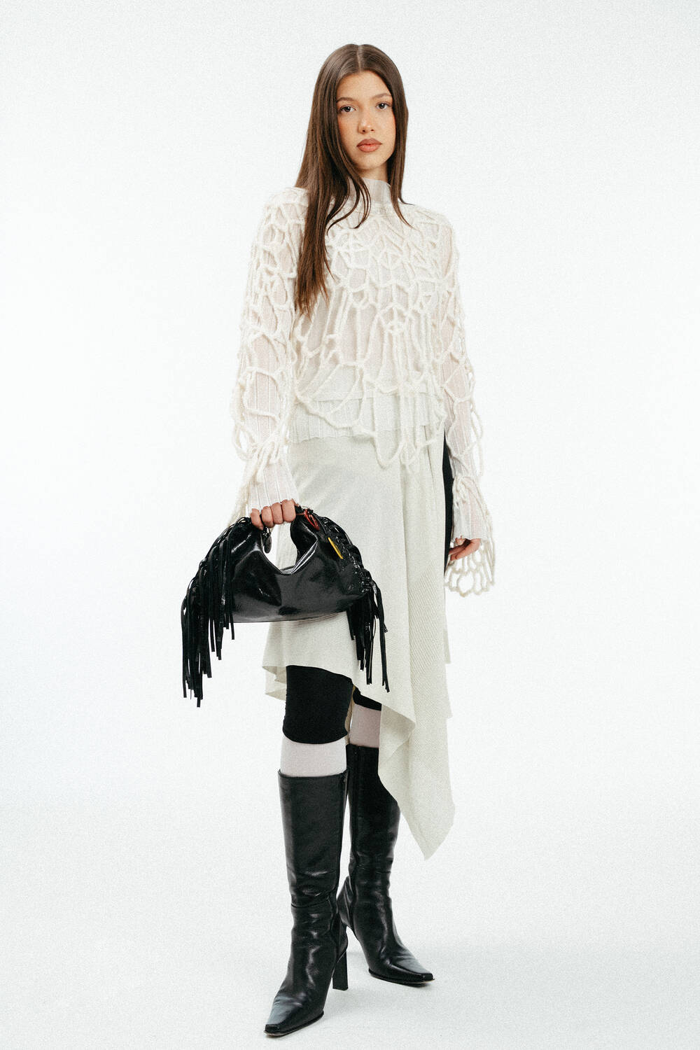 Weiblich gelesenes Model in losem, weißen Strick, mit schwarzer Ledertasche mit Fransen in der Hand