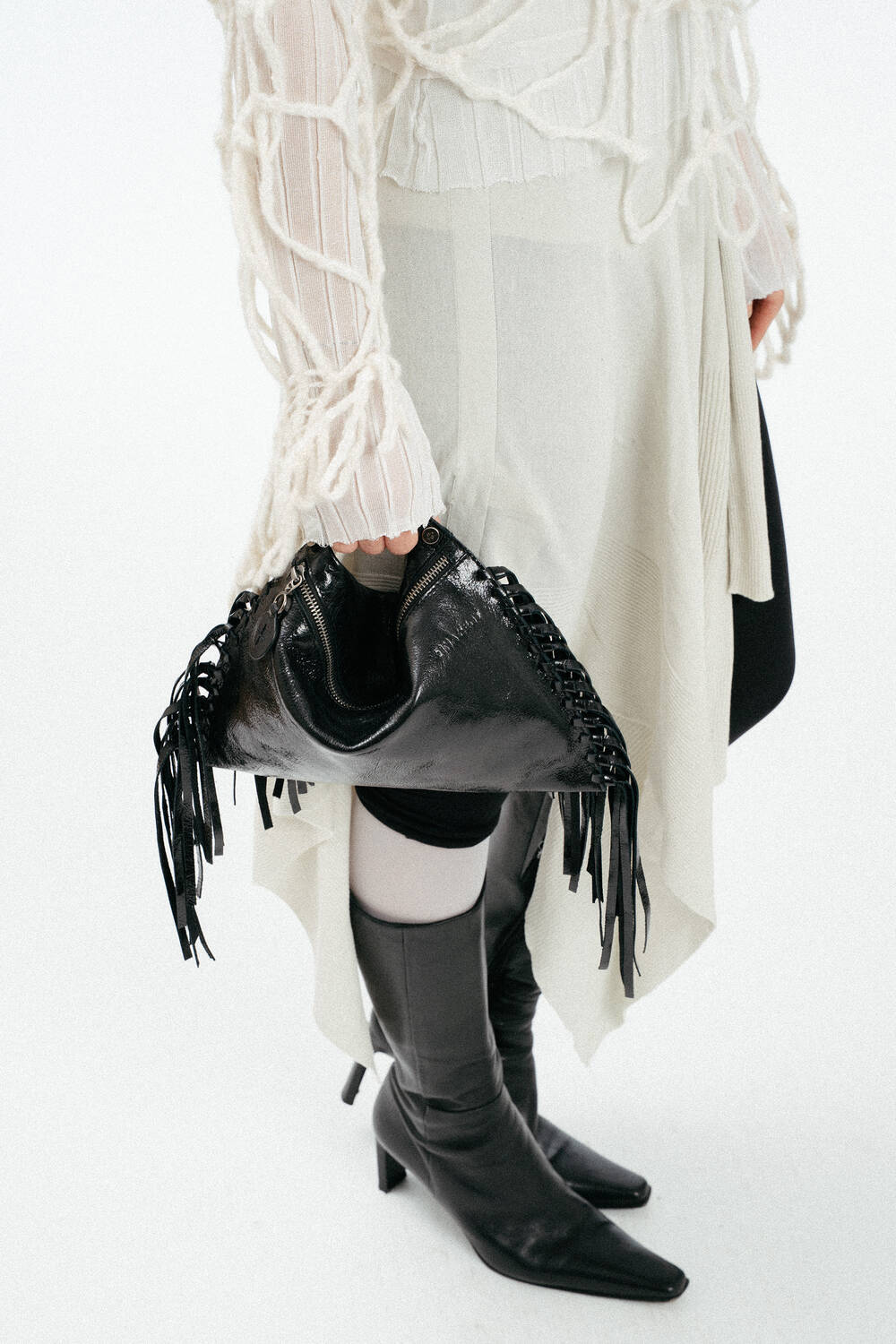 Schwarze, Ledertasche mit Fransen, gehalten von einem weiblich gelesenen Model