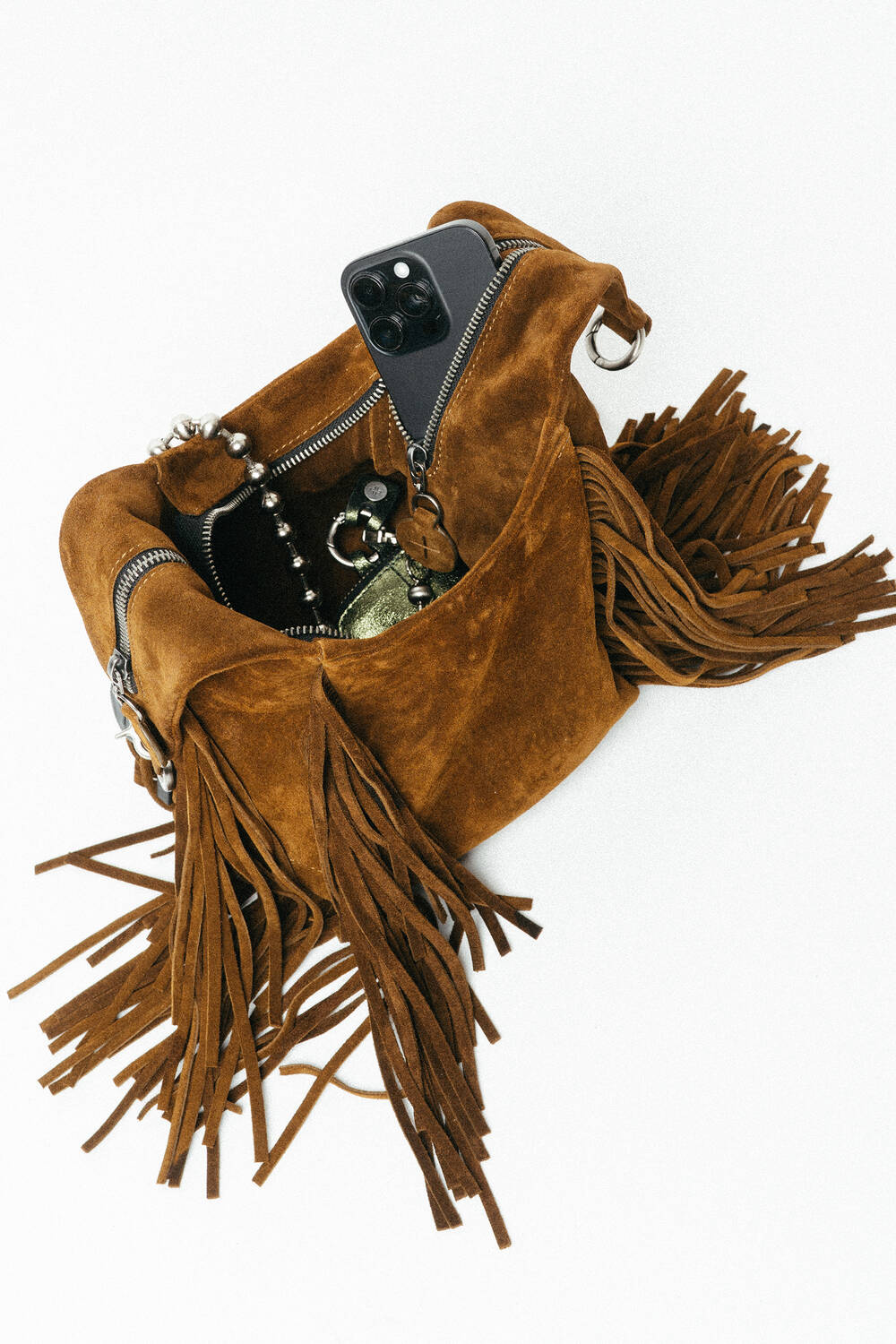 An INA KENT brown suede fringe handbag with a phone, keys, and jewelry partially visible inside.