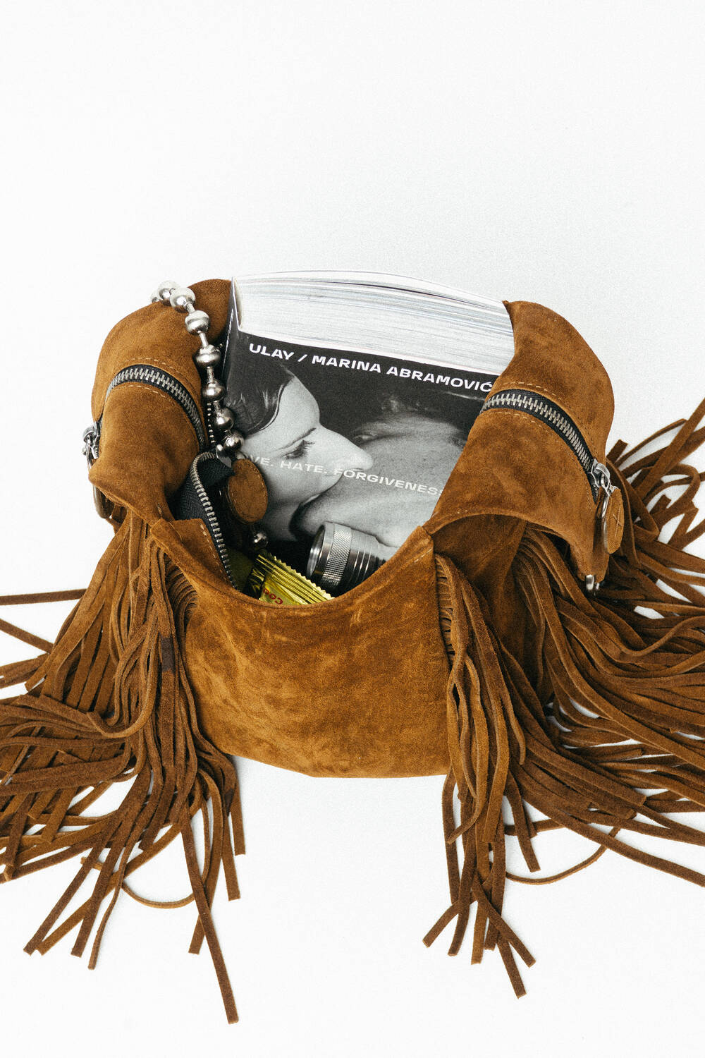 Brown suede fringe bag by INA KENT with zippers, containing a Ulay/Marina Abramović book, a camera, a beaded bracelet, and a yellow item inside.