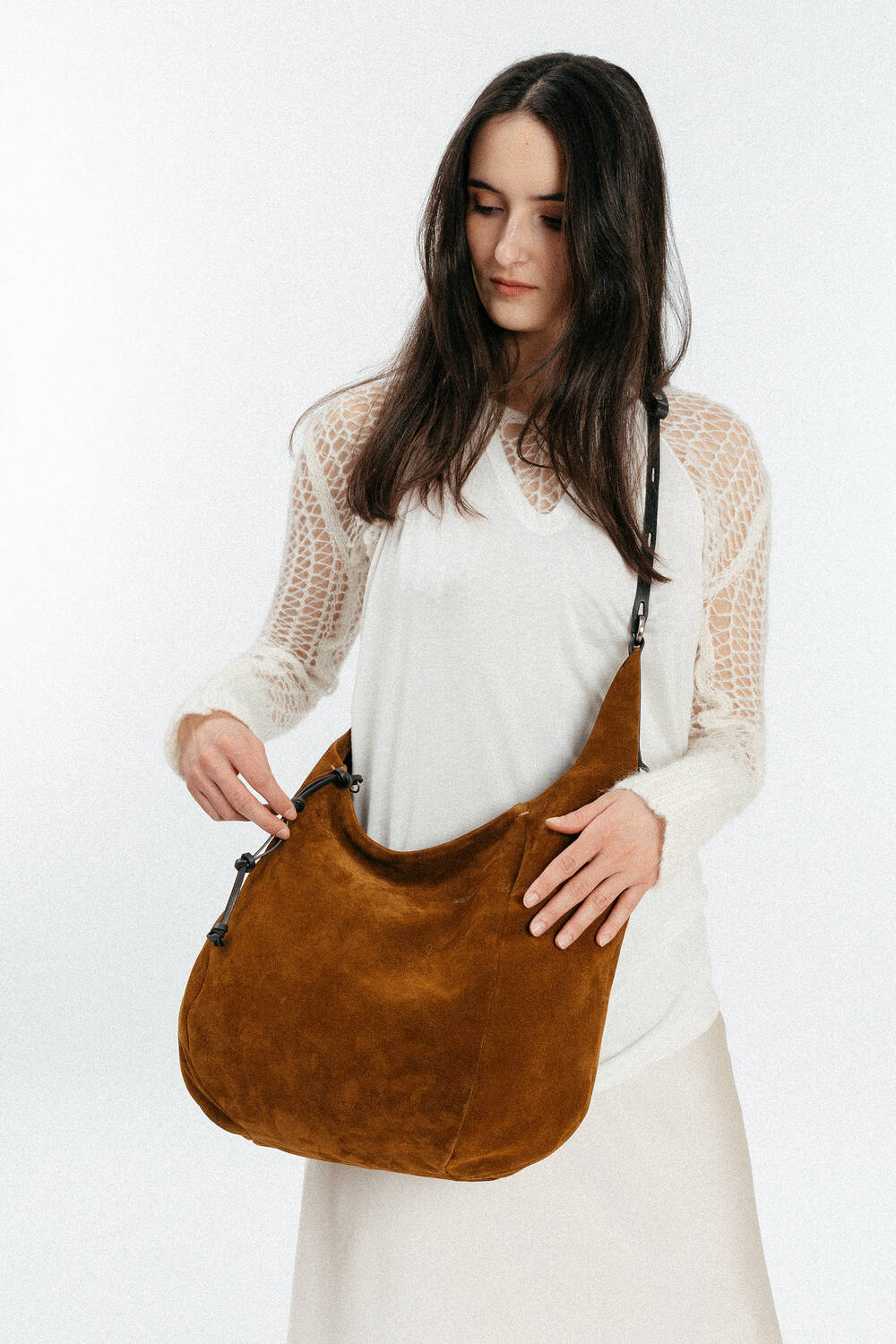 A woman with long dark hair wearing a white outfit holds a large brown INA KENT suede shoulder bag against a plain light background.