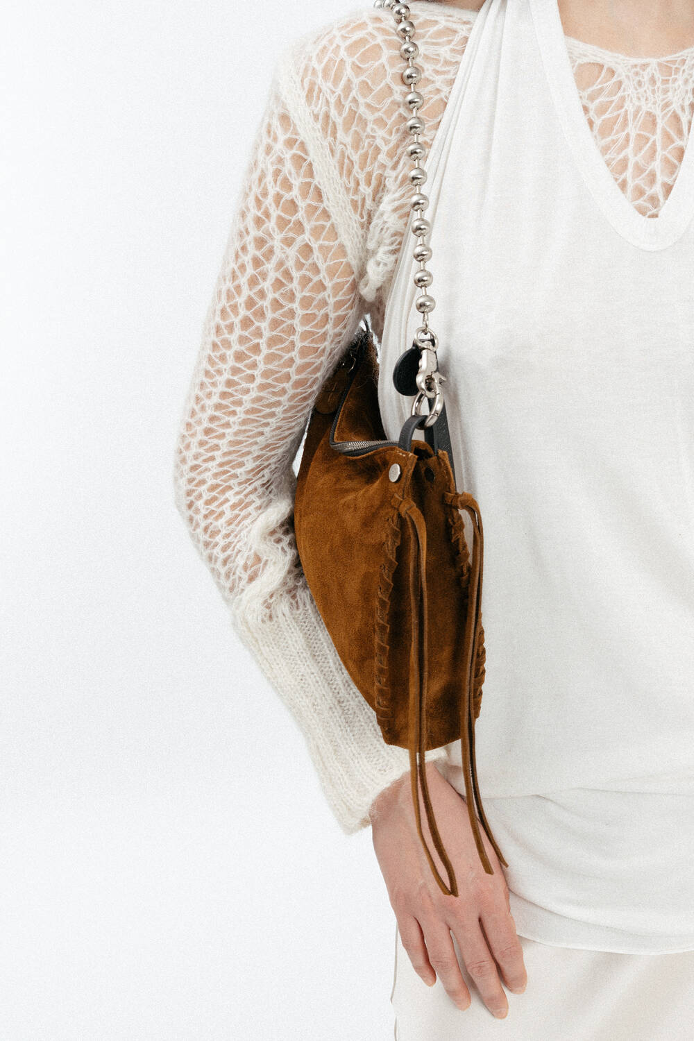 Person wearing a white knit top and holding an INA KENT brown suede shoulder bag with a chain strap.