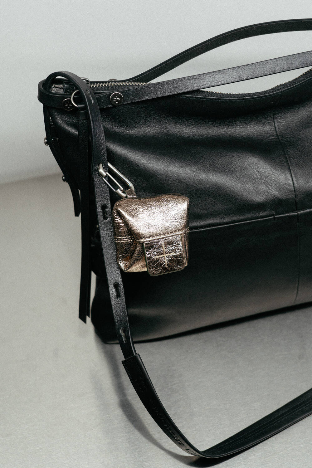 Black leather shoulder bag by INA KENT with a long strap, featuring a small metallic pouch attached to the strap.