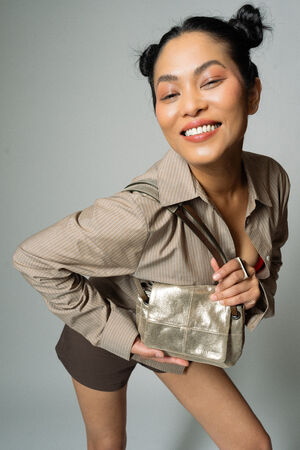 Person smiling while posing with hands on knees, wearing a striped shirt and holding a small metallic INA KENT handbag.