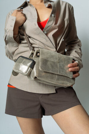 Person wearing a striped beige shirt, red top, and brown shorts, holding a chic INA KENT grey suede handbag.