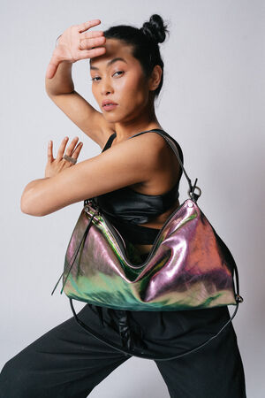A person posing with a large iridescent INA KENT handbag, wearing a black top and pants, with hair styled in two buns against a plain background.