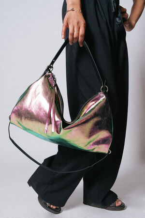 Person holding a large iridescent INA KENT handbag in their right hand, wearing black pants and sandals.