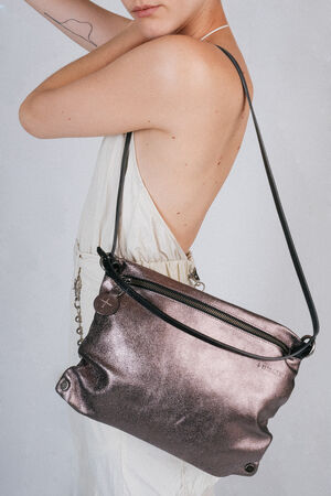 Person in a white dress with an exposed back, holding an INA KENT metallic shoulder bag. The bag has a zipper and a black strap and is carried on the person's left shoulder.