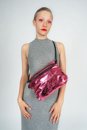 Person with short hair and bright pink eye makeup wearing a gray sleeveless dress, holding a shiny pink INA KENT handbag with a black strap.