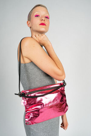 Person with short hair wearing a grey dress, holding an INA KENT metallic pink purse with a black strap over their shoulder, and wearing bright pink eye makeup.