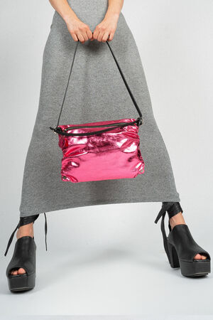 A person holding a shiny pink INA KENT bag against a gray dress. The person is wearing black platform shoes.