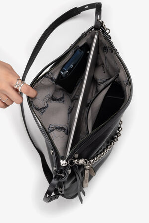 A person points to the interior of an open black handbag from INA KENT, revealing a partially visible electronic device pocket, a pen, and a keychain attached to the zipper pull.