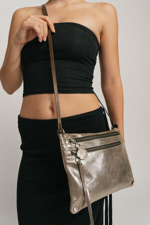 A person wearing a strapless black top and skirt holds an INA KENT metallic crossbody bag with two zippered pockets and a shoulder strap.