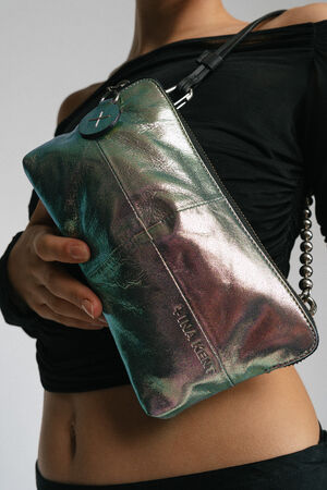 A person in a black top holds an INA KENT metallic holographic handbag with a circular charm and a chain strap.