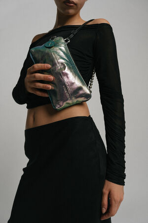 A person is wearing a black off-the-shoulder top and black skirt, holding an INA KENT metallic iridescent clutch bag with a chain strap across their torso.