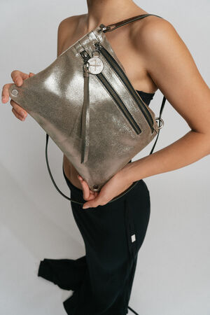 Person holding a metallic, triangle-shaped crossbody bag with zippers and a decorative charm by INA KENT. The individual is wearing a black outfit.