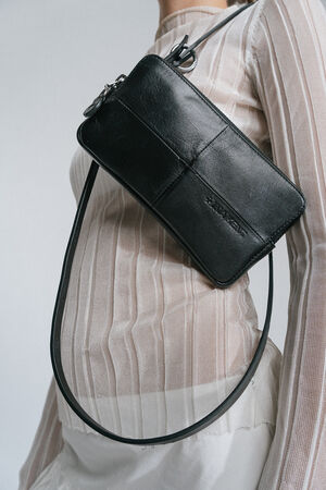 A person is wearing a long sheer white top with an INA KENT black leather crossbody bag slung over their shoulder.