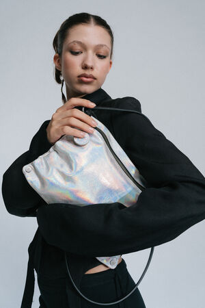 A person wearing a black outfit holds an INA KENT silver holographic bag against a plain background.