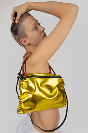 Person with short hair poses holding an INA KENT shiny yellow with black straps over their shoulder. The background is plain and bright.