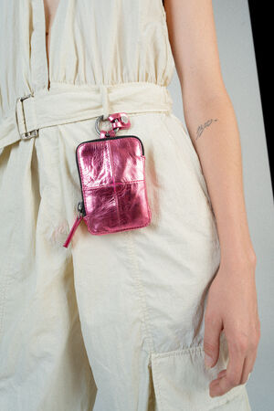 A person wearing a light-colored belted dress with a metallic pink square pouch from INA KENT attached to the belt. A small tattoo is visible on the person's arm.