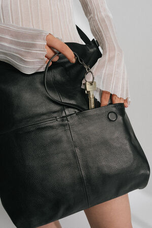 A person wearing a white striped sweater places a key attached to a keyring into the front pocket of their sleek black INA KENT leather bag.